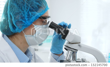 Female scientist analyzing sample through microscope, wearing protective lab gear during medical research investigation. Medicine, healthcare and science concept Female scientist analyzing sample through microscope, wearing protective lab gear during medical research investigation. Medicine, healthcare and science concept 132145700