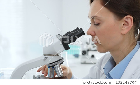 Female scientist examining samples through a microscope in a modern lab, conducting pharmaceutical research and developing treatments. Medicine, healthcare and science concept Female scientist examining samples through a microscope in a modern lab, conducting pharmaceutical research and developing treatments. Medicine, healthcare and science concept 132145704