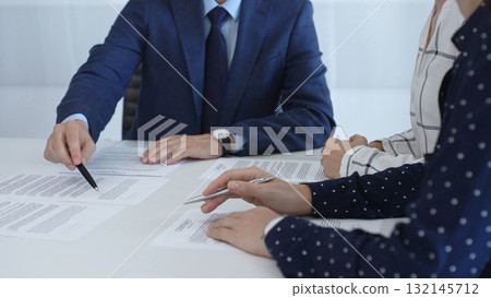 Business professionals analyzing contract details, gesturing with pens while discussing legal terms during collaborative meeting, focused on negotiation process Business professionals analyzing contract details, gesturing with pens while discussing legal terms during collaborative meeting, focused on negotiation process 132145712