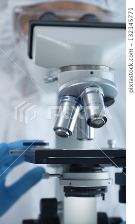 Medical virologist in a hazmat suit, mask, and gloves, diligently working at a microscope in a laboratory researching viruses. Healthcare and science concept 132145771