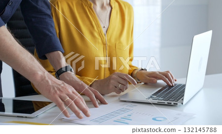 Business colleagues collaborating on a project while analyzing financial charts and entering data on a laptop in a modern office. Businesspeople concept 132145788