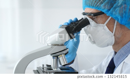 Male scientist wearing protective gear examining microscope slide, analyzing research sample in sterile laboratory environment. Health care and science concept 132145815