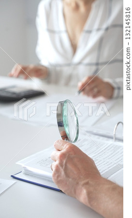 Groupe of professional accountants working together, using a magnifying glass and a calculators, to audit financial reports in their brightly lit office. Audit and taxes concept Groupe of professional accountants working together, using a magnifying glass and a calculators, to audit financial reports in their brightly lit office. Audit and taxes concept 132145816