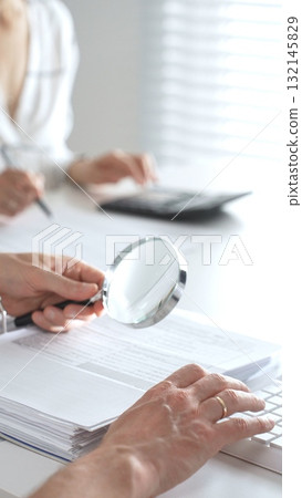 Group of accountants are working together, using a magnifying glass and a calculator, to audit financial reports in office. Audit and taxes in business Group of accountants are working together, using a magnifying glass and a calculator, to audit financial reports in office. Audit and taxes in business 132145829