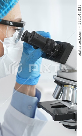 Scientist woman wearing gloves and a mask uses a microscope in a laboratory setting, conducting important research and analysis, close up. Medicine and science concept 132145833
