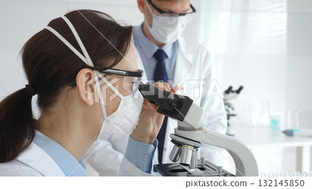 Two scientists, a man and a woman, in lab coats and protective gear, conduct research in a sterile laboratory. Concept of medicine and science 132145850