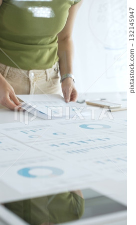 Businesswoman pointing at financial charts and graphs on a table, with a pie chart on a flip chart in the background. Business people concept Businesswoman pointing at financial charts and graphs on a table, with a pie chart on a flip chart in the background. Business people concept 132145947