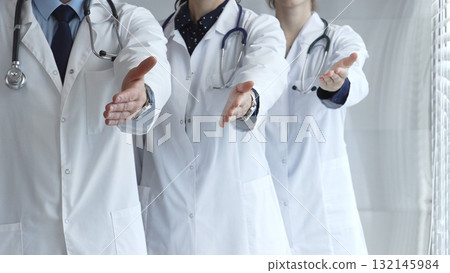 Medical professionals team offering welcoming handshake, ready to greet and assist with healthcare and patient support, establishing trust in hospital environment 132145984