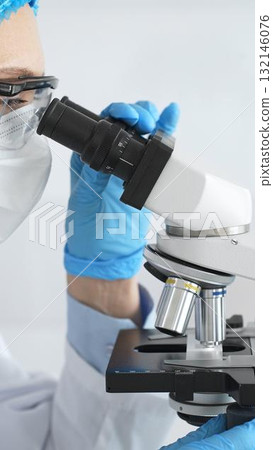 Female scientist in blue gloves and mask using microscope in laboratory setting, conducting important research and analysis, close-up. Medicine and science concept 132146076