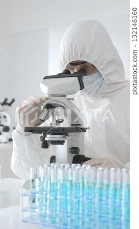 A medical virologist in protective gear examines viral samples under a microscope while conducting research in a laboratory setting A medical virologist in protective gear examines viral samples under a microscope while conducting research in a laboratory setting 132146160