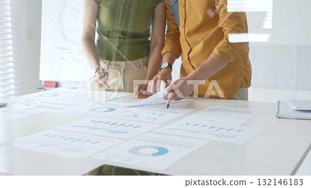 Business professionals analyzing financial reports, pointing at charts during collaborative meeting, discussing data with focused professional demeanor 132146183