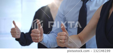 Business people team showing thumbs up gestures in a row, expressing approval, agreement, success, and full support for a project or strategy in a corporate office setting with sun flair 132146199