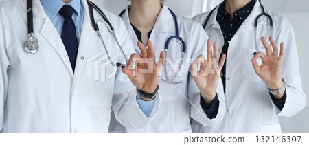 Medical team in white coats with stethoscopes making ok gestures, conveying teamwork, confidence, successful care and trust in a hospital or clinic setting Medical team in white coats with stethoscopes making ok gestures, conveying teamwork, confidence, successful care and trust in a hospital or clinic setting 132146307