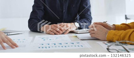 Business people team analyzing financial data and discussing growth strategy during meeting, pointing at charts and graphs, taking notes in modern office Business people team analyzing financial data and discussing growth strategy during meeting, pointing at charts and graphs, taking notes in modern office 132146325