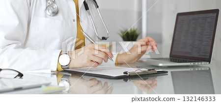 Doctor working on medical records, writing prescription in clinic office, using laptop for patient data management. Medicine, healthcare and science concept 132146333