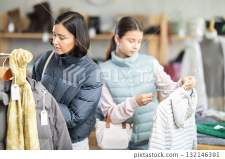 Mother and teen daughter looks at products in store and selects coat or jacket for child 132146391