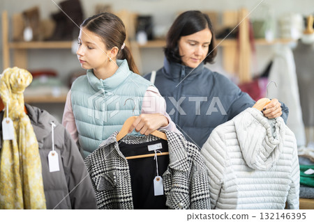 Teenage girl with her mother chooses coat or down jacket Teenage girl with her mother chooses coat or down jacket 132146395