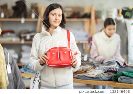 Woman looks at products in store and selects handbag. Woman looks at products in store and selects handbag. 132146408