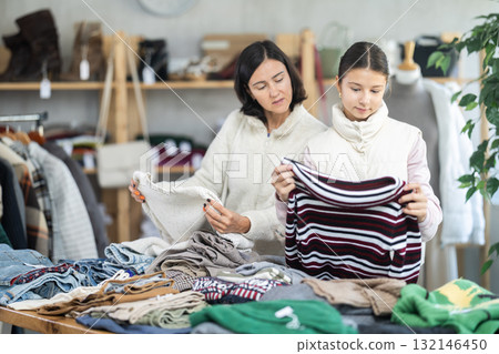 Mother and teen daughter looks at products in store and selects knitted jumper. 132146450