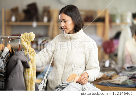 Adult woman chooses coat or down jacket in clothing store Adult woman chooses coat or down jacket in clothing store 132146465