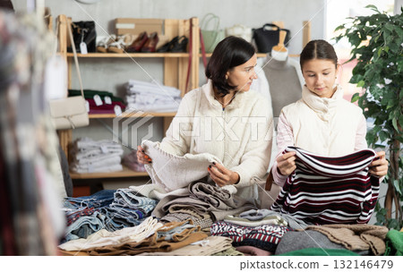 Mother and teen daughter looks at products in store and selects knitted jumper. Mother and teen daughter looks at products in store and selects knitted jumper. 132146479
