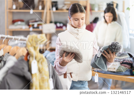 Teen girl looks at products in store and selects hat. Family shopping Teen girl looks at products in store and selects hat. Family shopping 132146517