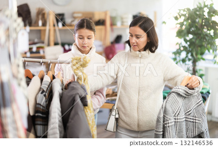 Mother and teen daughter looks at products in store and selects coat or jacket. Mother and teen daughter looks at products in store and selects coat or jacket. 132146536