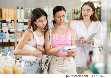 Attentive mother and daughter buyers choosing medical ointment and professional female parmacist helping in pharmacy 132146688