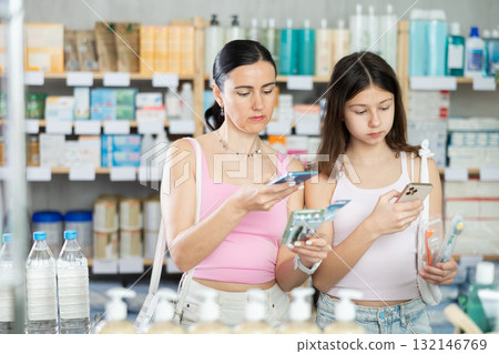 Positive happy mother and daughter buyers at pharmacy holding and choosing best toothbrush, scan QR code 132146769