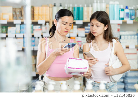woman with her daughter scans a pack of pads on her phone 132146826