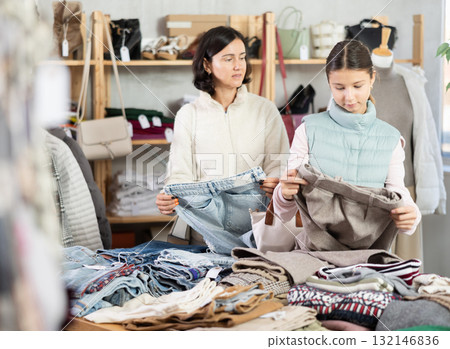 Mother and teen daughter looks at products in store and selects trousers 132146836