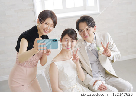 Bride and groom taking photos with friends on smartphone 132147626