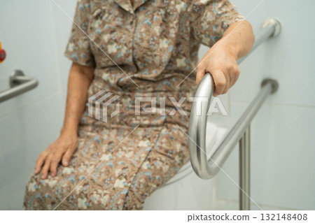Asian elderly woman patient use toilet support rail in bathroom. 132148408