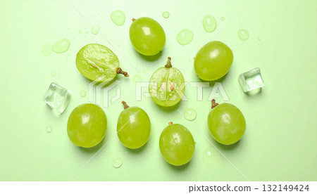 Flat lay of fresh green grapes, ice, and water drops on a pastel green background. 132149424