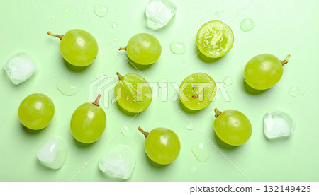 Flat lay of fresh green grapes, ice, and water drops on a pastel green background. 132149425