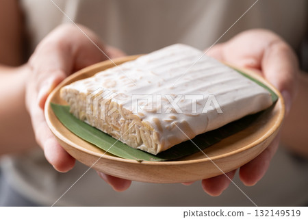 Tempeh made from fermented soybeans on wooden plate holding by hand, Traditional Indonesian food 132149519