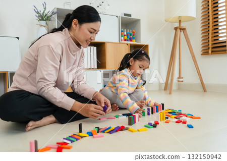toddler girl and mother playing colorful wooden block toy or domino game together toddler girl and mother playing colorful wooden block toy or domino game together 132150942