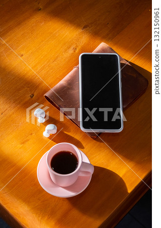 Smartphone, white earbuds and coffee cup on wooden table. 132150961