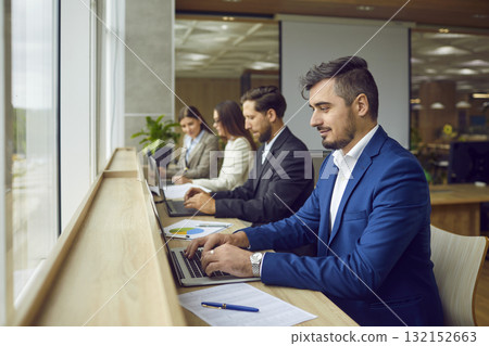Business people sitting in a row and working on laptop computers in modern open plan office. 132152663