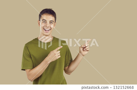 Smiling happy teenager boy pointing to copy space and looking at camera on beige background. Smiling happy teenager boy pointing to copy space and looking at camera on beige background. 132152668