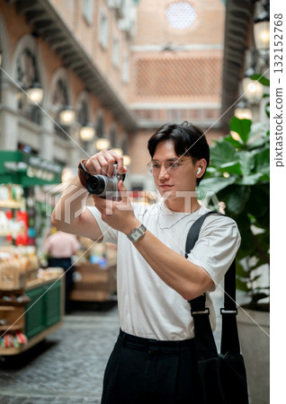 Asian man wearing glasses in white tee taking photos on his camera in shopping mall or indoor market 132152768
