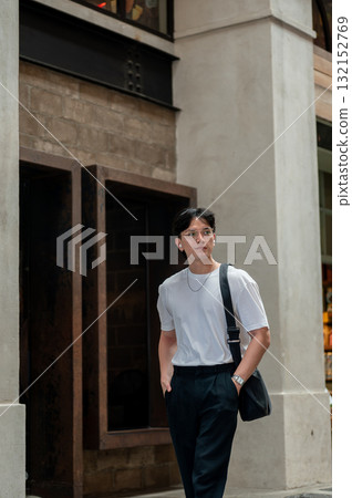 Asian man with glasses in white tee walking around with hands in pocket in shopping mall or building 132152769