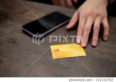 Close up of a hand placing a yellow credit card next to a smartphone on wooden table. Card payment. 132152782