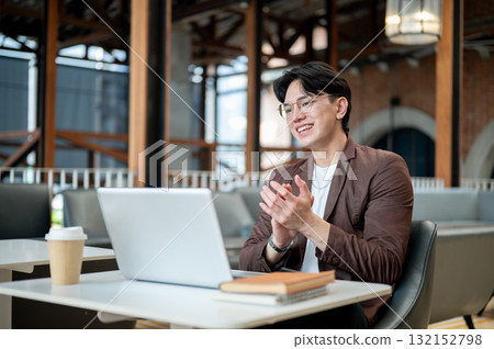 Brown suit asian man with glasses clapping his hands to his laptop. Online meeting or presentation. 132152798