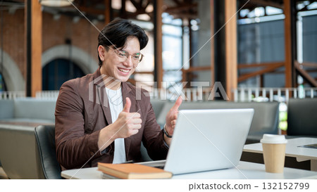 Brown suit asian man with glasses is giving thumbs up to his laptop. Online meeting or presentation. Brown suit asian man with glasses is giving thumbs up to his laptop. Online meeting or presentation. 132152799