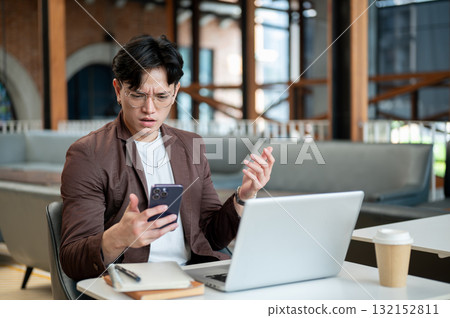 Brown suit asian man with glasses is stunned as he look at his smartphone. Bad news or Shocking info Brown suit asian man with glasses is stunned as he look at his smartphone. Bad news or Shocking info 132152811