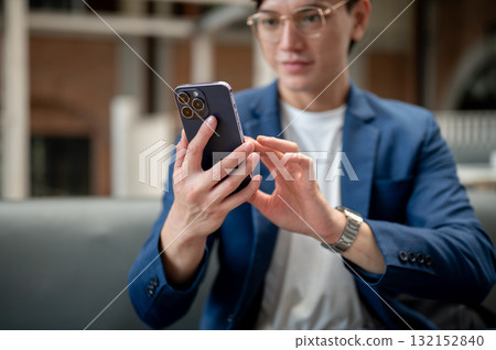 Close up of a blue suit man looking and typing on his smartphone, sitting in cafe or coffee shop. Close up of a blue suit man looking and typing on his smartphone, sitting in cafe or coffee shop. 132152840