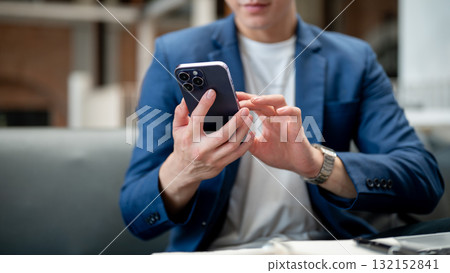 Close up of a man in blue suit looking and typing on his smartphone, sitting in cafe or coffee shop. 132152841