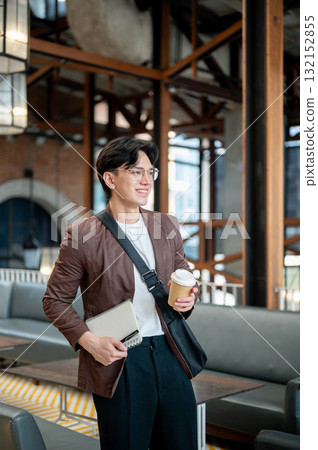 Brown suit man with glasses standing while holding a coffee cup and notebook in cafe or coffee shop. Brown suit man with glasses standing while holding a coffee cup and notebook in cafe or coffee shop. 132152855