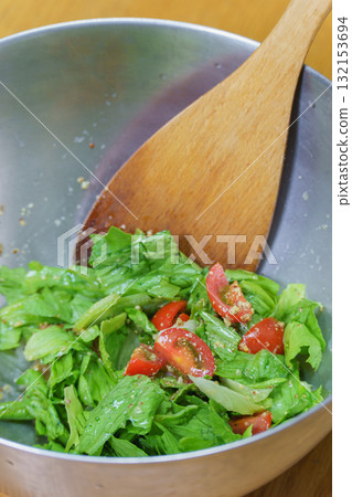 Mixing salad in a bowl with a wooden spoon | Lettuce and tomato salad 132153694